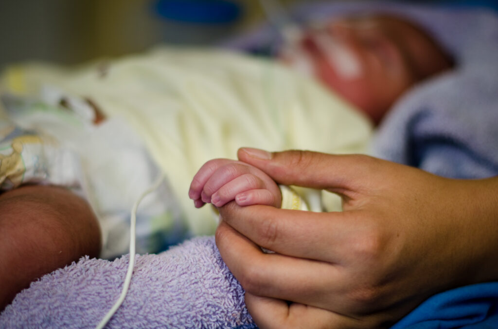 Close-up of a hand holding a patient's hand in a hospital bed.