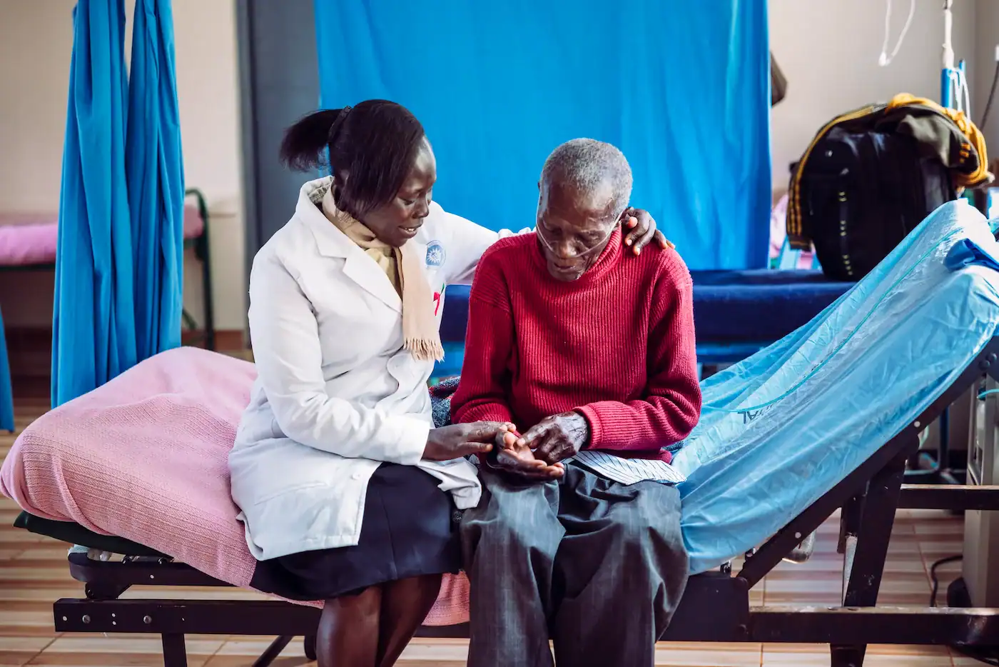 Female nurse in white coat praying with and comforting an elderly male patient in a hospital ward