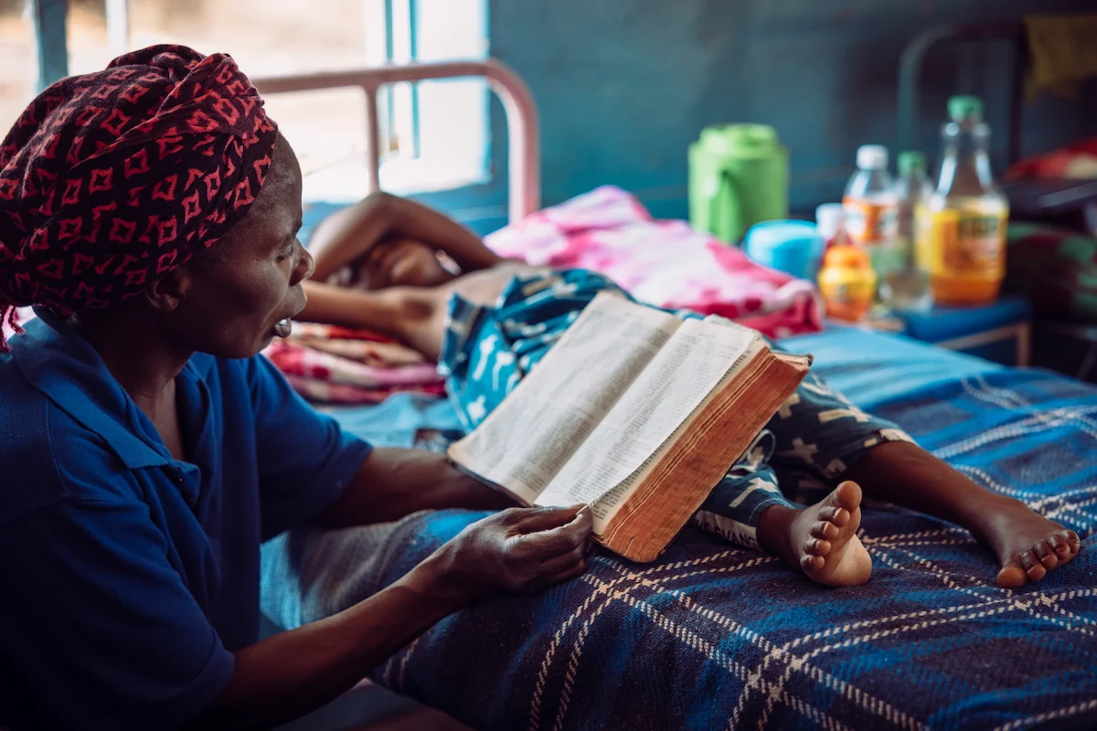 Mother reading the Bible aloud to her child in a hospital bed