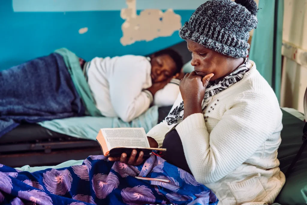 Woman reading the Bible at the bedside of a resting hospital patient